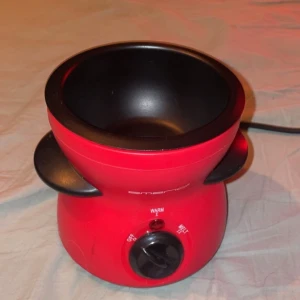 Emerio Chokladfondue - Emerio chokladfondue i röd färg, perfekt för dessert och fest. Utrustad med avtagbar skål, två värmelägen (Warm/Melt) och enkel kontroll. Skålen är i gott skick med mindre repor, och apparaten är fullt fungerande. Perfekt för smältning av choklad och servering.