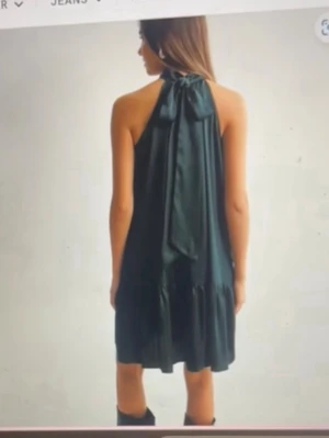 Svart omlottklänning med volang - Supersnygg svart kortklänning med halterneck och knyt i nacken. Klänningen har en lös passform och volang nedtill som ger en cool och trendig look. Perfekt för dig som gillar stilrena och enkla plagg med en twist. Materialet känns lätt och har ett fint fall. flowigt material. köpt från nelly men från neo noir  och i storlek 36!  har alldrig användt den har prislappen kvar och allt! en väldigt mörkblå färg!