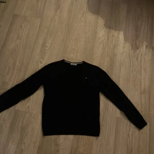 Svart tröja från J.Lindeberg, S - Svart långärmad tröja från J.Lindeberg i storlek M. Dessvärre har den krympt i tvätten så jag skulle uppskatta storleken till en Small. Tröjan har en rund hals och ett litet broderat J.Lindeberg-logo på bröstet. Perfekt för dig som gillar stilrena och klassiska plagg.