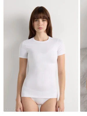 Vit tight t-shirt i bomull - Säljer en klassisk vit t-shirt med tight passform och rund hals. T-shirten har korta ärmar och är tillverkad i mjuk bomull, perfekt för en clean och enkel stil.
