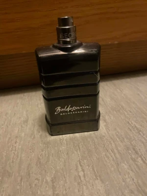 Stilren Baldessarini herrparfym - En elegant parfym från Baldessarini i en mörk, stilren flaska. Perfekt för dig som vill sticka ut med en klassisk och modern touch. Märket står för kvalitet och exklusivitet. Volym och ingredienser syns ej på bilderna.
