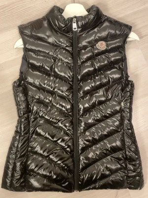 Svart dunväst från Moncler - Snygg svart dunväst med märket moncler, köpt på blocket så är inte säker om den är äkta. Säljes pga för liten. Skavanker finns på bilden annars är den i bra skick💕 sitter som en XS-S