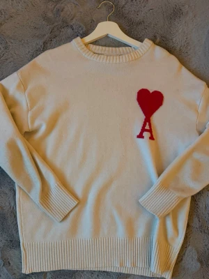 Ami tröja S - Säljer en beige stickad tröja från Ami med röd hjärta.  Jättebra skick 10/10. Säljer den eftersom jag har slutat att använda den. Kan diskutera om priset! 