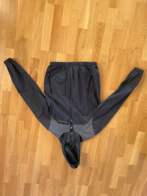 Svart vindjacka från McKenzie - Svart och mörkgrå vindjacka från McKenzie med huva och hel dragkedja framtill. Jackan har två sidofickor med dragkedja och elastiska muddar vid ärmslut och midja. Perfekt för blåsiga dagar och har en clean, sportig look.