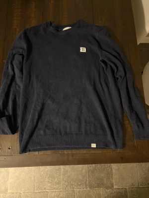 Mörkblå stickad tröja Les Deux M - Snygg mörkblå stickad tröja från Les Deux i storlek M. Tröjan har rund hals, ribbade muddar och en liten broderad patch med 'II' på bröstet. 