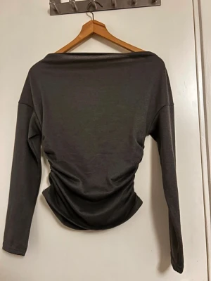 Mörkgrå långärmad topp från SHEIN - Säljer en mörkgrå långärmad topp från SHEIN i storlek S. Toppen har en tight passform med bred halsringning och är tillverkad i mjuk polyester med lite stretch. Snyggt rynkad i midjan för en cool siluett. Perfekt att styla med jeans eller kjol.