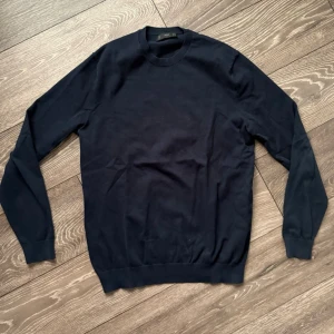 Mörkblå tröja från MNG MAN - Snygg mörkblå tröja från MNG MAN i klassisk modell med rund hals och långa ärmar. Tröjan är tillverkad i mjuk bomull och har ribbade muddar vid hals, ärmslut och nederkant. Perfekt för dig som gillar stilrena och enkla plagg. Lite urtvättad 