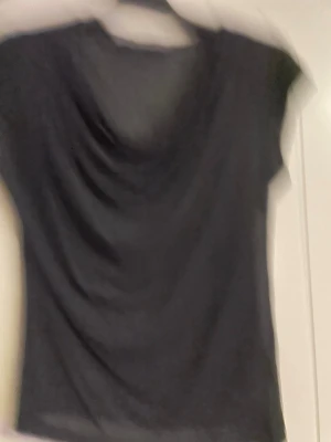 Svart topp från Tiger of Sweden - Säljer en svart topp från Tiger of Sweden med draperad front och korta ärmar. Tunn och mjuk känsla, perfekt att styla med jeans eller kjol. Enkel och stilren design som funkar till många looks.