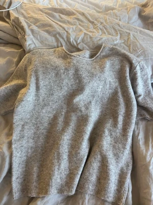 Grå stickad kortärmad tröja - Mysig grå stickad tröja med korta ärmar och rund hals. Perfekt för lager-på-lager och chill dagar. Ribbstickade detaljer vid ärmslut och nederkant ger en snygg finish. Enkel att matcha med jeans eller kjol.