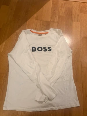 Vit långärmad topp från BOSS - Säljer en vit långärmad topp från BOSS med svart logotyptryck på bröstet. Aldrig använd 