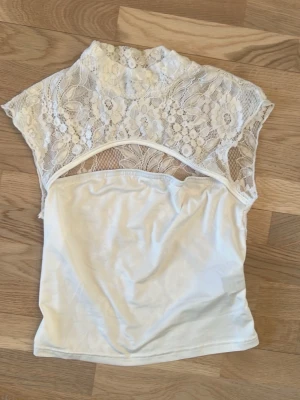 Vit spetsblus med blommönster - Säljer en vit blus med genombruten spets upptill och blommönster. Nedre delen är slät och mjuk, medan överdelen är helt i spets. 