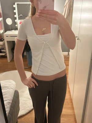 Vit omlottopp med knappar från Bik Bok - Säljer en vit omlottopp från Bik Bok i storlek XS. Toppen har korta ärmar, v-ringning och dekorativa knappar framtill. Den är croppad och gjord i mjuk bomull, perfekt för en chill och stilren look.