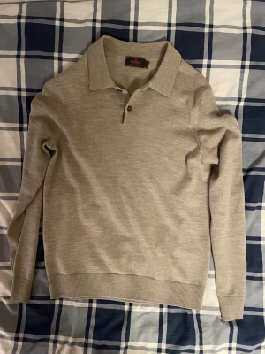 Beige pikétröja i merinoull från Morris - Säljer en beige pikétröja från Morris i 100% merinoull. Tröjan har klassisk krage, två knappar vid halsen och ribbade muddar vid ärmslut och nederkant. Perfekt för dig som gillar stilrena och mjuka plagg med lång ärm.