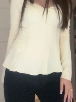 Ljusgul långärmad peplumtop - Säljer en ljusgul peplumtop med lång ärm och snygg v-ringad hals. Toppen har en figurnära passform upptill och ett utsvängt avslut som ger en feminin siluett. Perfekt att styla med jeans eller kjol för en trendig look.