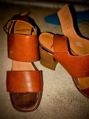 Bruna sandaler med klack från Vagabond - Säljer ett par snygga bruna sandaler från Vagabond med breda remmar i skinn och stabil klack. Modellen har öppen tå och en fyrkantig form framtill. Perfekt för dig som gillar stilrena och klassiska skor med lite höjd.