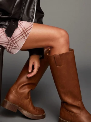 Bruna höga boots från Bershka - Säljer ett par snygga bruna boots från Bershka med rund tå och platt sula. Skorna är höga och tillverkade i skinnimitation med stilrena sömmar och en klassisk siluett. Perfekta för dig som gillar en enkel men cool look.