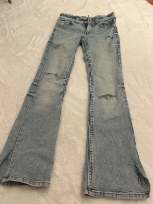 Bootcut jeans med låg midja från H&M - Snygga ljusblå bootcut jeans från H&M med låg midja och justerbar linning. Jeansen har slitna detaljer på benen och klassiska fem fickor. Materialet är mjukt denim i bomull, perfekt för en avslappnad look. 🥰