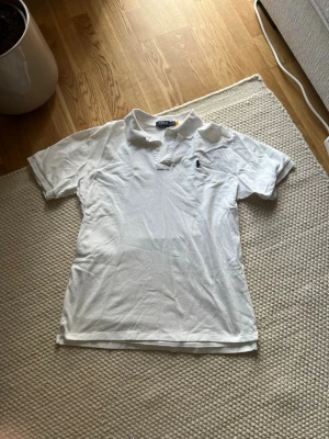 Vit piké från Polo Ralph Lauren XL - Säljer en klassisk vit pikétröja från Polo Ralph Lauren i storlek XL. Modellen är Custom Slim Fit med korta ärmar, krage och knappar framtill. Tröjan har den ikoniska broderade loggan i marinblått på bröstet och är tillverkad i bomull. OBS DU VET VARFÖR DEN ÄR BILLIG!