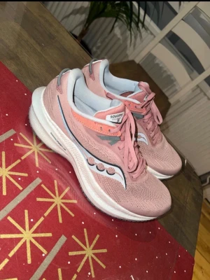 Saucony rosa sneakers med mesh - Säljer ett par Saucony sneakers i ljusrosa med vit och grå sula. Skorna har mesh-ovandel för bra andningsförmåga, snörning och Sauconys logga i vitt och grått på sidan. Perfekta för träning eller promenader, riktigt sköna och snygga.