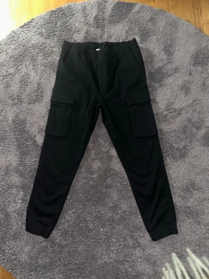 Svarta cargopants - Helt nya cargopants frå Cubus. Den är helt oanvänd och är i storlek L. Nypris: 500kr, Mitt Pris: 199kr. *Pris kan diskuteras vid snabb affär* Tveka inte med att ställa frågor! Jag svarar snabbt. Skickar ut inom 1 dag.