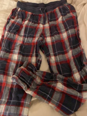 Rutig mjukisbyxa med snörning - Säljer ett par sköna mjukisbyxor i röd, blå och vit rutig design. Byxorna har elastisk midja med snörning och muddar vid bensluten. Perfekta för chill hemma eller häng med kompisar. Materialet är mjukt och bekvämt bomullstyg. Har även fickor på vardera bensida. 