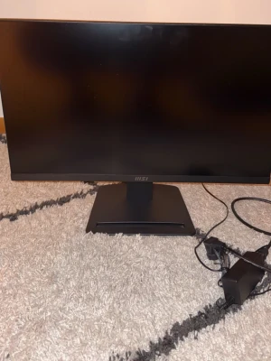 MSI PRO MP2412 - MSI PRO MP2412 är en 24-tums LED-skärm med HDMI och DisplayPort-anslutningar. Skärmen har en modern design och levereras med strömadapter. Några mindre dammfläckar syns på skärmen, men i övrigt ser den ut att vara i gott skick utan synliga skador.