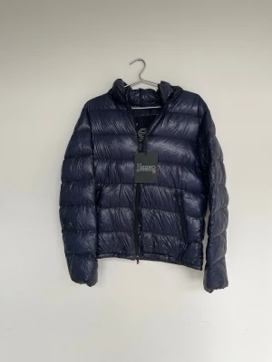 Herno Jacka - Navy blå dunjacka från herno i en väldigt populär glansig modell! Tags medföljer. Storlek S. Finns lagningar som syns på sista bilderna, syns knappt vid användning. Annars är skicket bra. Kontakta mig för fler frågor och funderingar!