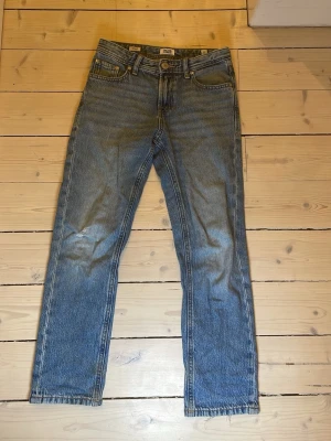 Blå jeans från Jack & Jones - Säljer ett par klassiska blå jeans från Jack & Jones i modellen Regular Clark. Jeansen har fem fickor, raka ben och normal passform. Materialet är jeans i bomull och de har en snygg tvättad look med lite slitna detaljer vid benslutet.