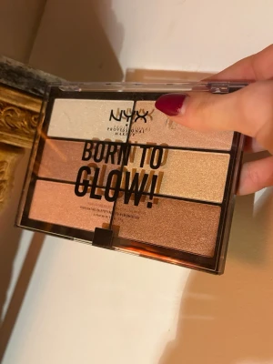 NYX Born To Glow Highlighter Palette OÖPPNAD - Säljer den TikTok-virala NYX Born To Glow highlighterpaletten (oöppnad) med sex skimrande nyanser i guld, champagne, koppar, rosa och pärlemor. Paletten har en genomskinlig plastförpackning och rektangulära pans. Perfekt för att skapa glow och highlighta ansiktet.