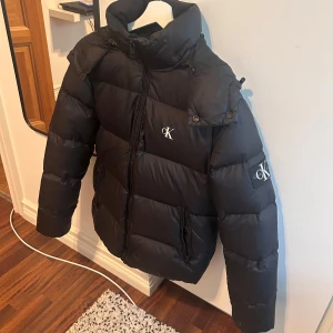 Svart pufferjacka från Calvin Klein  - Svart pufferjacka från Calvin Klein den är i storlek Xs vilket passar perfekt för dig som är mellan 165-175 cm den har en liten skada men inget stort hör av er vid frågor:)