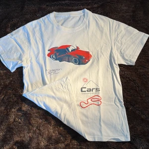Vit t-shirt med röd sportbil Cars-motiv - Vit t-shirt med tryck av en röd sportbil och texten 'A Collection about Cars'. T-shirten har rund hals, korta ärmar och en rak passform. Materialet är mjuk bomull och trycket har coola racing-vibbar. Perfekt för dig som gillar bilar och streetstyle. Modellen är 179 65kg så skulle säga att det är en S/M