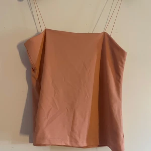 Persikofärgad linnetopp från Amisu - Säljer en stilren persikofärgad linnetopp från Amisu med tunna axelband. Toppen har en rak och enkel passform, perfekt för varma dagar. Tillverkad i mjukt material som känns skönt mot huden. Snygg att matcha med jeans eller kjol.