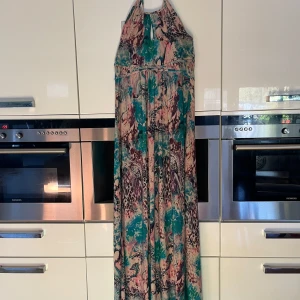 Långklänning Lise Sandahl med mönster - Säljer en maxiklänning från Lise Sandahl med färgstarkt mönster i turkos, rosa, beige och lila. Klänningen har halterneck och en snygg öppning fram vid halsen. Materialet är mjukt och följsamt, perfekt för dig som gillar unika prints och bohemisk stil.