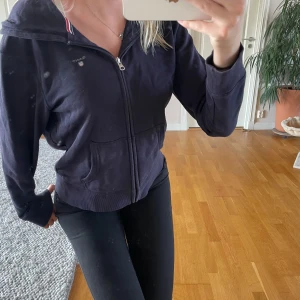 Mörkblå hoodie från Gant med dragkedja - Mörkblå hoodie från Gant med dragkedja framtill och huva. Klassisk design med två fickor och ribbade muddar. Snygg detalj med röd, vit och blå rand på insidan av kragen. Perfekt för en lugn och stilren look. Färgen är lite urtvättad annars är den i väldigt bra skick!💗