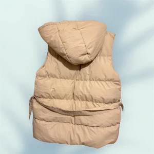 Beige dunväst med huva och bälte - Beige quiltad dunväst från bohoo med huva och bälte i midjan. Västen har tryckknappar framtill och två fickor. Perfekt för hösten ganska skön och bekväm 🍂🍁😍