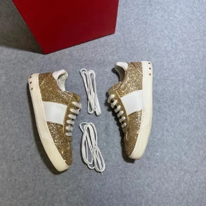 Valentino Flycrews glittriga sneakers guld - Säljer ett par Valentino Rockstud sneakers med glittrig guldglitter på ovandelen och vita paneler. Skorna är i storlek 37. Skorna har vita snören, platt sula och dekorativa nitar på hälen. Märkeslogga på plösen och insidan. Perfekt för dig som vill sticka ut med lyxig stil.