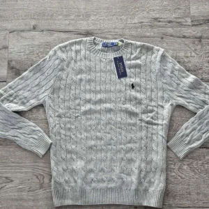 stickad tröja Polo Ralph Lauren - Kabelstickad grå tröja från Polo Ralph Lauren. Läng: 60 cm Axel bredd: 40 cm