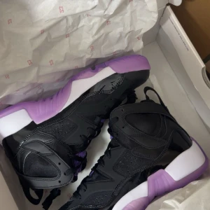 Svarta sneakers med lila detaljer - Snygga svarta sneakers med högt skaft och lila samt vita detaljer på sulan. Skorna har snörning och är tillverkade i en mix av skinn och syntetmaterial. Perfekta för dig som vill sticka ut med en unik färgkombination.