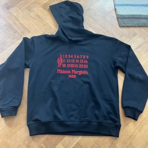 Svart Mason margiela hoodie - Riktigt skön och stilren hoodie från Mason margiela. Den är bara använd ett antal gånger och har inga tecken på användning. Riktigt fet och unik design perfekt nu till de kallare dagarna! Hör av er om frågor om pris eller allt annat!