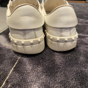 Valentino Garavani vita sneakers - Tjena, Säljer ett par snygga Valentino Garavani sneakers i vitt skinn med bred svart rem över foten och coola nitar på hälen storlekk 40,5. Köpta på NK i Stockholm 5999kr, tyvärr medföljer ingen låda då den hivats pga flyttning, skick 7,5/10!! ”priset går självklart att diskuteras” Tveka inte på att höra av dig vid eventuella frågor  eller funderingar🤝🏻