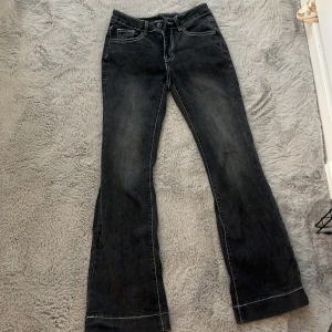 Svarta bootcut jeans med kontrastsömmar - Snygga svarta jeans med bootcut passform och vita kontrastsömmar. Klassisk femficksmodell med dragkedja och knapp framtill. Jeansen har en lätt tvättad look och är tillverkade i jeansmaterial.