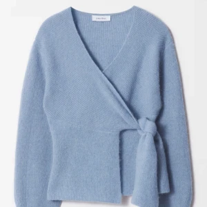 Blå omlottkofta från & Other Stories - Superfin ljusblå omlottkofta från & Other Stories i mjuk stickad kvalitet. Koftan har v-ringning, långa ärmar och knyt i sidan för en snygg och trendig look. Perfekt att slänga på sig när det är lite kyligare ute.