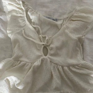 Vit blus med snörning - Säljer en söt vit kortklänning från lager 157 med volangärmar och snygg snörning framtill. Klänningen har en rundad öppning vid bröstet och är gjord i ett lätt, krinklat bomullstyg som ger en chill vibe. Perfekt för varma dagar och sommarhäng!