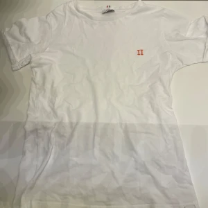 Vit Les Deux t-shirt 146-152cm - Vit t-shirt i bomull med korta ärmar och en orange logga på bröstet. Enkel och clean design som passar till det mesta. Skön passform och rund halsringning. Mvh Hannes!