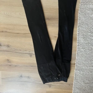 Svarta mjukisbyxor med fickor - Svarta mjukisbyxor i mjukt sammetstyg med resår i midjan och snörning framtill. Byxorna har raka ben och två stora fickor med knappar bak. Perfekta för en chill och avslappnad stil.