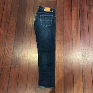 Helt nya Levi jeans  - Helt nya och oanvända Levi's 502 Premium jeans i mörkblå tvätt med klassiska fem fickor, gul kontrastsöm och läderpatch bak. Modellen har en rak och något avsmalnande passform, tillverkad i slitstarkt jeanstyg. Perfekta för dig som gillar en tidlös och clean look.