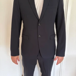 Mörkblå kostym (byxa, kavaj) från Tiger of Sweden - Snygg mörkblå kostym från Tiger of Sweden med klassisk kavaj och matchande byxor. Kavajen har två knappar, smala slag och fickor med lock. Använda ca 2 gånger. Storlek 52 på både byxor och kavaj. 