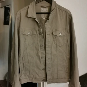 Beige jeansjacka från Jack & Jones - Stilren beige jeansjacka från Jack & Jones i klassisk modell med knappar framtill, två bröstfickor med lock och två sidofickor. Jackan har en rak passform och är tillverkad i bomull, perfekt för en avslappnad look.