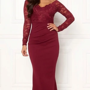 Vinröd långklänning med spets - Säljer en vinröd långklänning med snygga spetsdetaljer upptill och långa ärmar. Klänningen har en figurnära passform och v-ringad hals. Har endast haft den en gång. Köpte den ny för 999kr