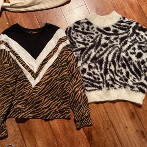 Två mönstrade tröjor med djurprint - Säljer två coola tröjor! Ena med brunt och svart tigerprint, vita detaljer och lång ärm. Den andra är en fluffig stickad tröja med svartvitt zebramönster och hög krage. Perfekta för dig som gillar djurmönster och vill sticka ut. L-XL.